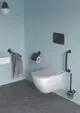 Schwarzer Griff an einer Wand im Badezimmer, befestigt neben einer Toilette von Ideal Standard. Im Hintergrund eine hellblaue Wand und grauer Bodenbelag.